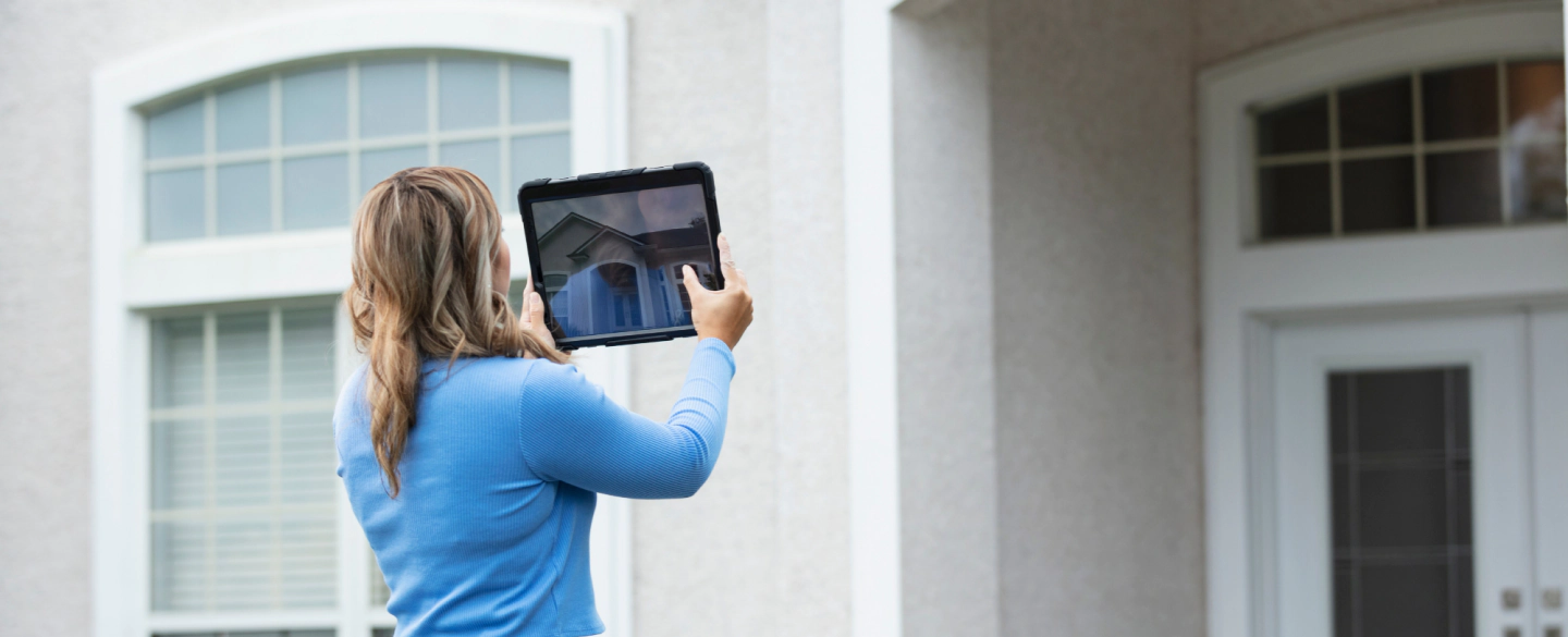 woman taking a picture of a beige house with glass windows
